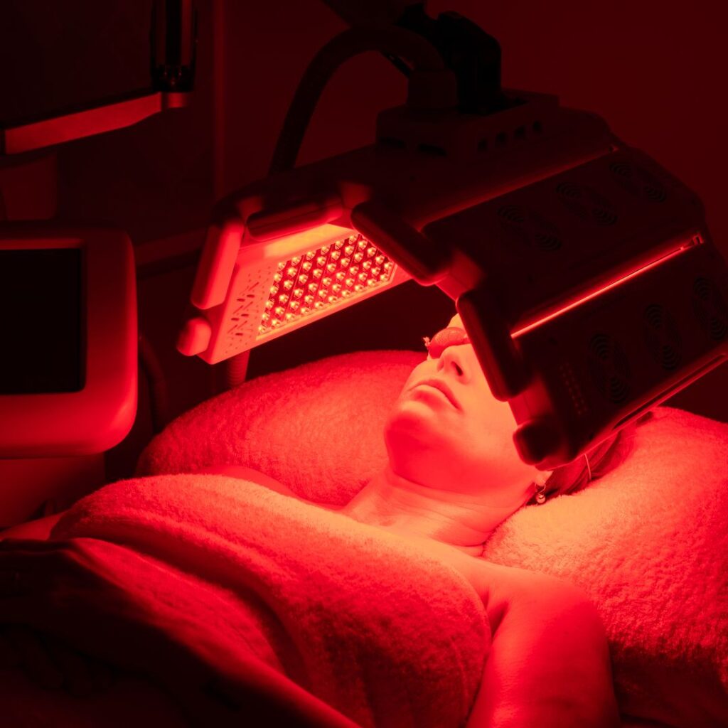 a person lying in a salon bed with a red LED light