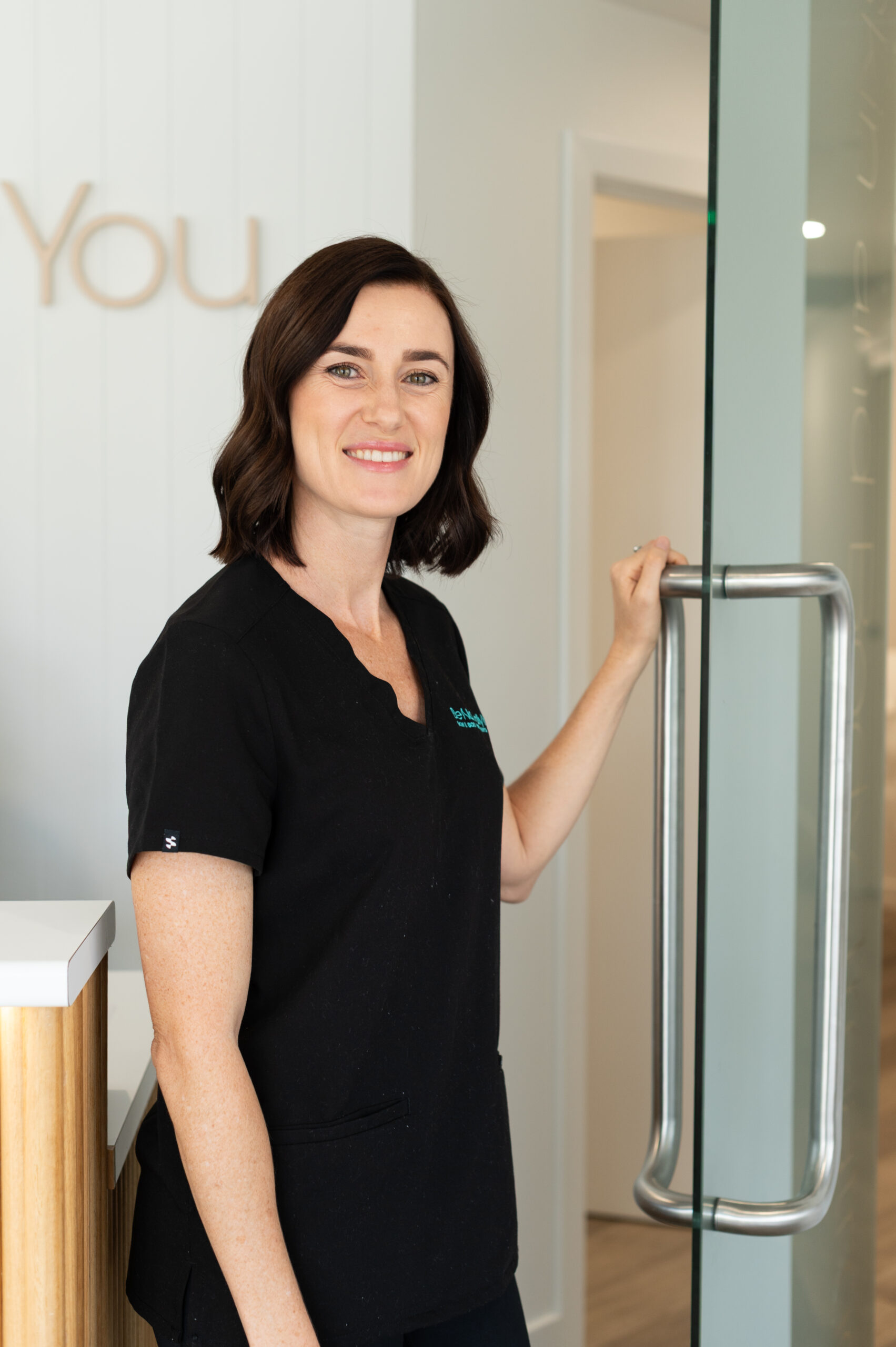 a woman in black scrubs standing by a glass door